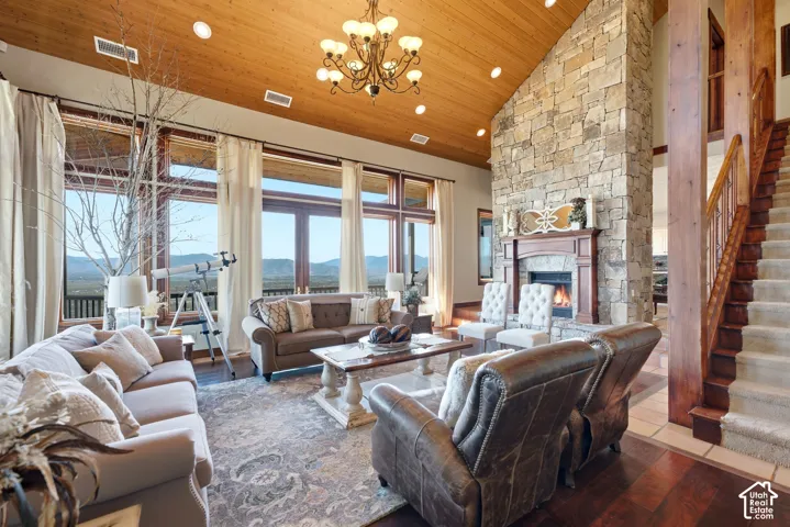 Great room featuring a vaulted wood-paneled ceiling, floor-to-ceiling windows, a stone fireplace with a wood mantel, wood-finish flooring, and a carpeted staircase with wood railing