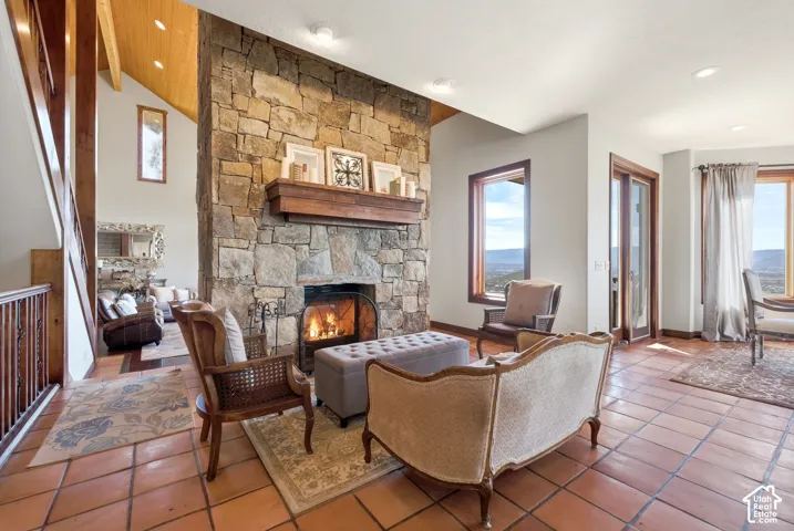 Stone fireplace with a substantial wood mantel, vaulted wood-paneled ceiling, recessed lighting, terra cotta tile flooring, and large windows with wood trim