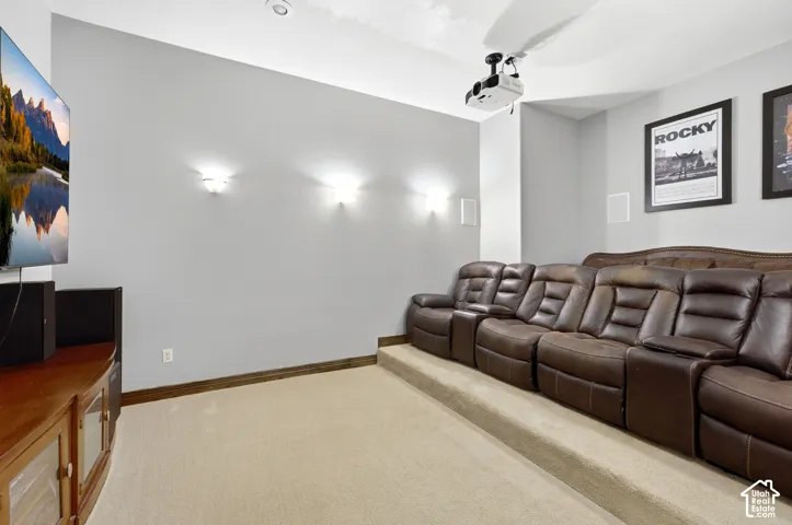 Dedicated media room featuring tiered flooring, recessed ceiling lighting, wall sconces, ceiling-mounted projector, and wall-mounted speakers