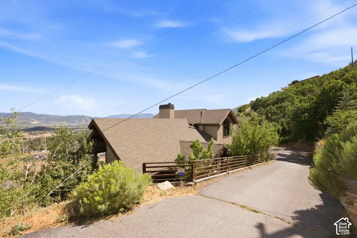 Multi-level residence featuring a brown shingle roof, chimney, and a natural wood fence