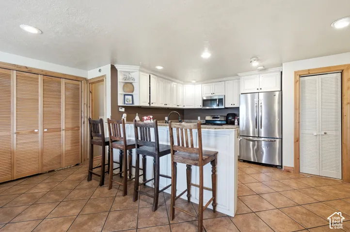 Kitchen featuring white cabinetry, stainless steel appliances, a breakfast bar, and tile flooring