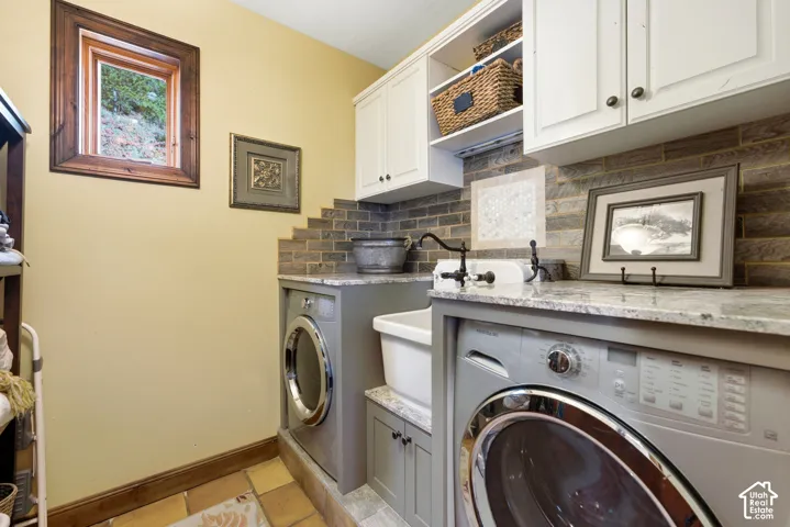 Utility room featuring dual front-loading machines, a white laundry sink, and light-toned cabinetry