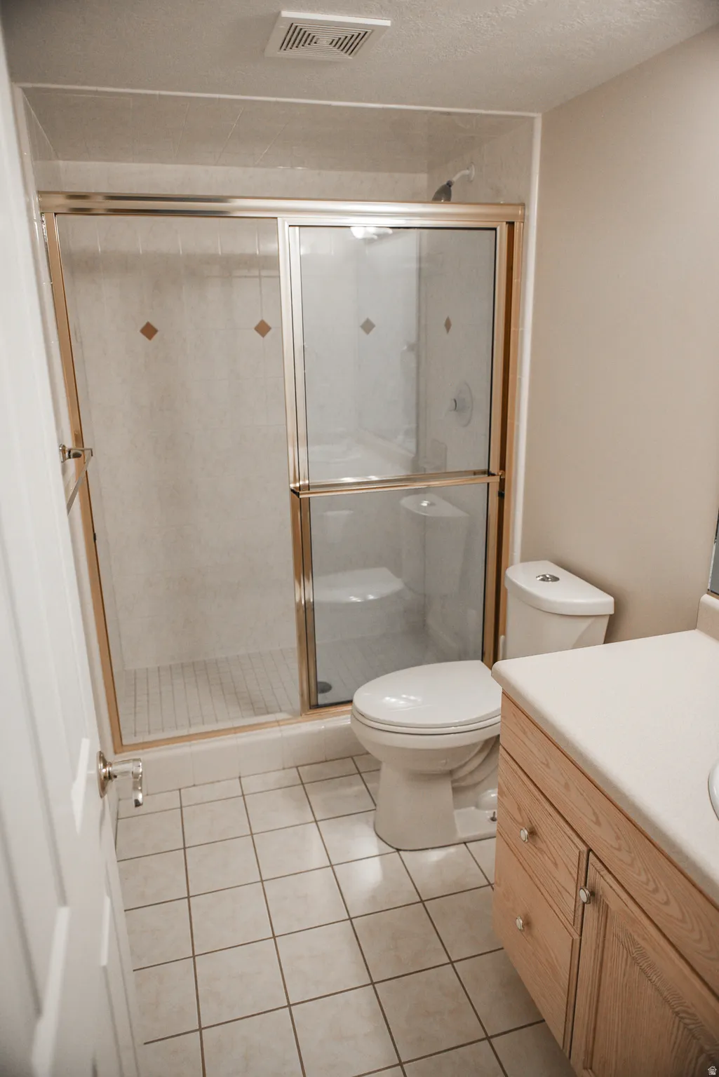 Bathroom featuring a shower with gold-toned framed glass doors, a single vanity with wood cabinetry, and square ceramic tile flooring