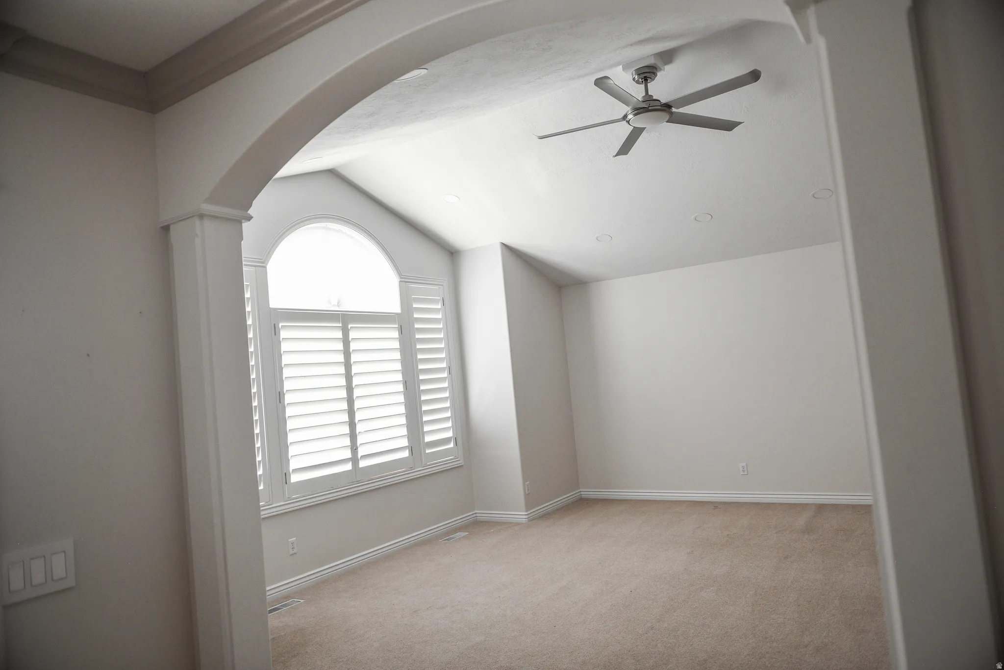 Vaulted ceiling room featuring a large arched window with plantation shutters, ceiling fan, recessed lighting, and neutral carpet flooring