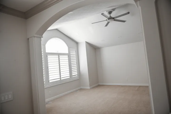 Vaulted ceiling room featuring a large arched window with plantation shutters, ceiling fan, recessed lighting, and neutral carpet flooring