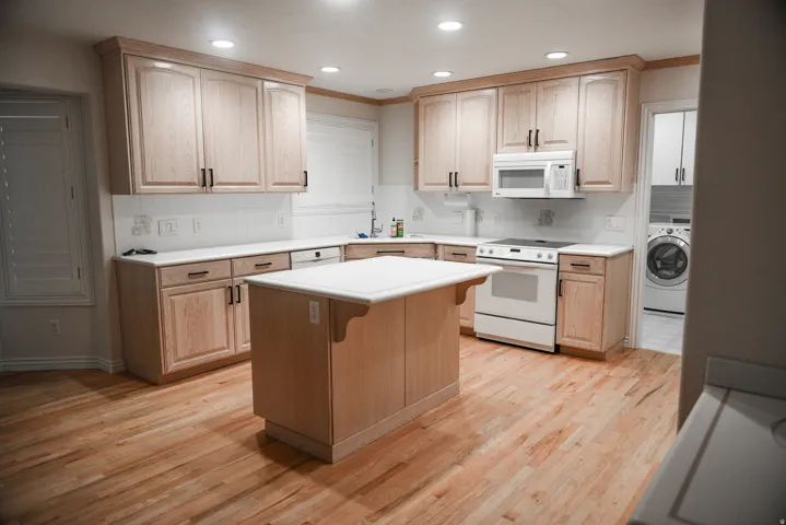 Kitchen featuring an island, wood-finish flooring, light wood cabinetry, white countertops, and a white subway tile backsplash