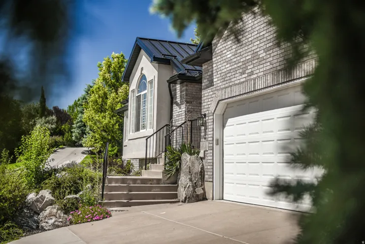 Stucco and brick exterior featuring a white paneled garage door, dark metal roof, arched window, and concrete steps with black metal railing