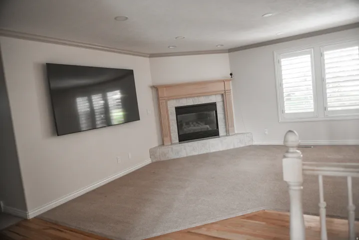 Living area featuring a gas fireplace with a wood mantle and tile surround, recessed lighting, and plantation shutters