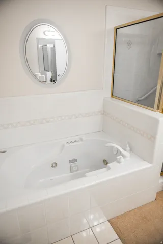 Soaking tub with white tile surround featuring decorative accent tile and a wall-mounted oval mirror
