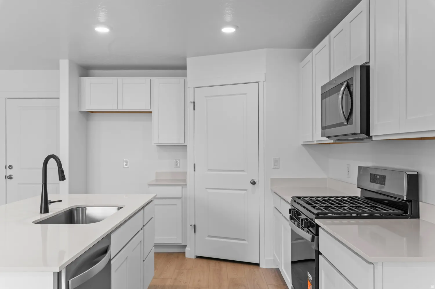 Bright kitchen featuring white cabinetry, light-toned countertops, stainless steel appliances, a center island with an undermount sink, and wood-finish flooring