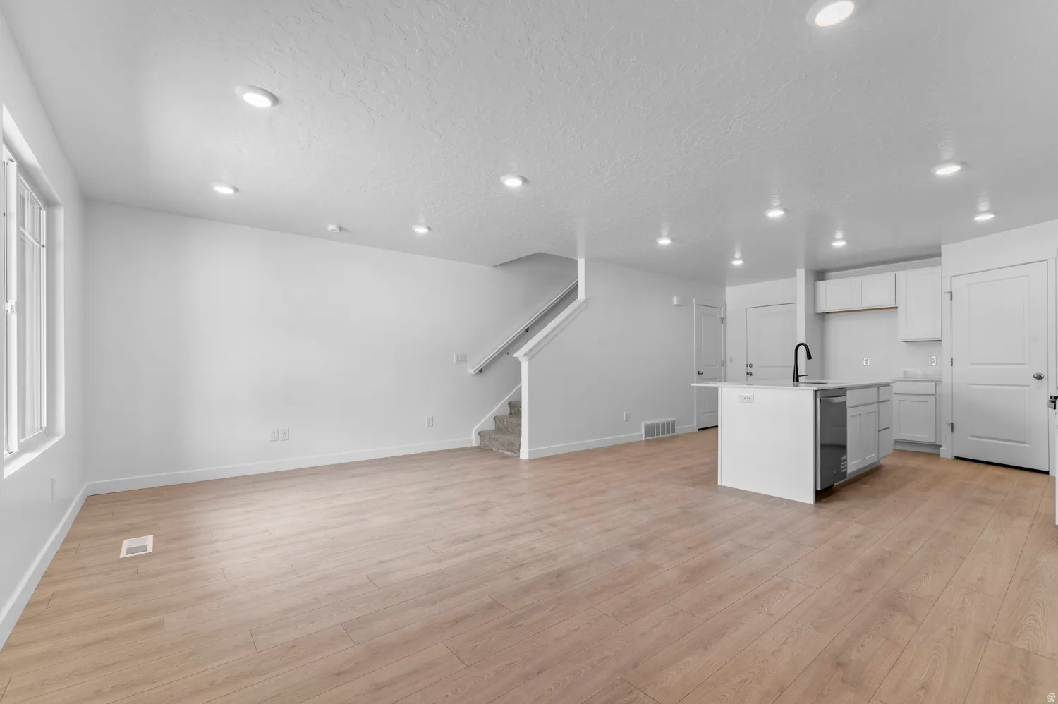 Open-concept living space featuring wood-finish flooring, recessed lighting, and a modern kitchen island with an integrated sink and black faucet