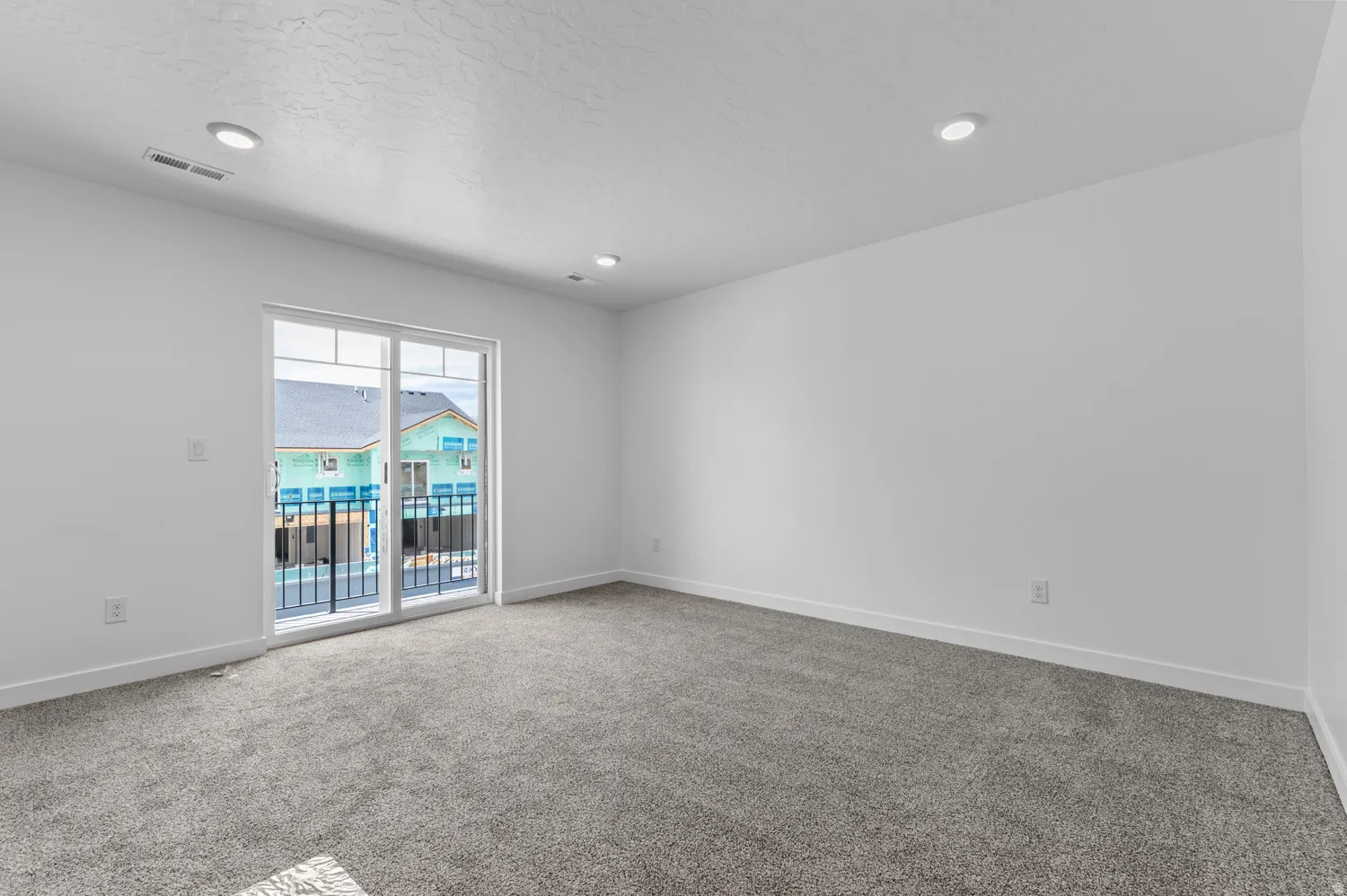 Carpeted room featuring white walls, recessed lighting, and a sliding glass door opening to a private balcony with black metal railings