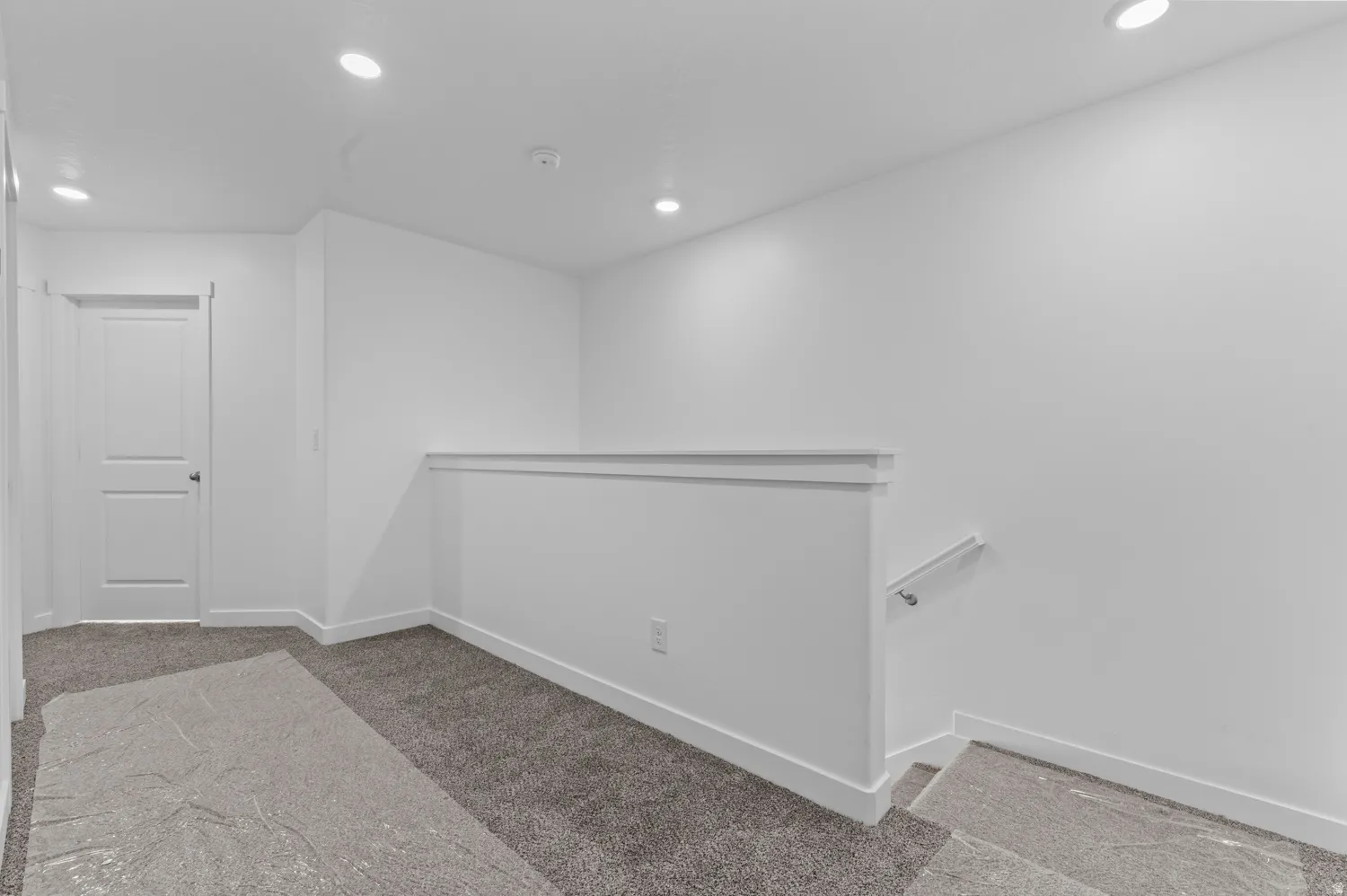 Upper-level landing featuring recessed lighting, a two-panel interior door, and a staircase with a handrail