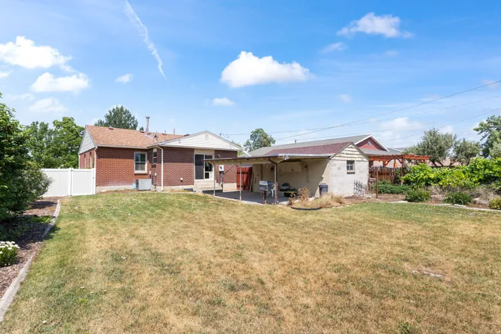 Spacious outdoor area featuring a red brick dwelling, an additional outbuilding with a covered patio, and a white vinyl privacy fence