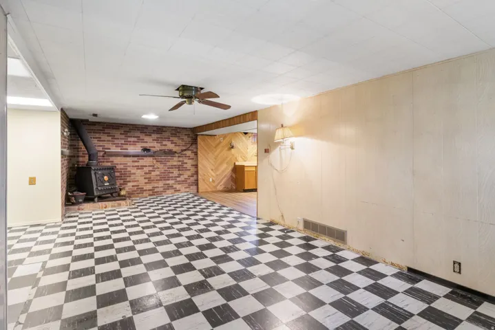 Spacious room featuring checkerboard flooring, a brick accent wall, and a cast iron stove