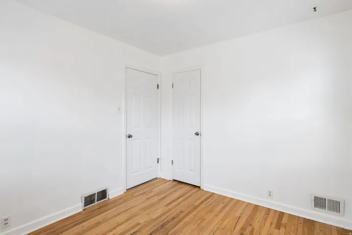 Hardwood flooring showcasing a natural wood-finish, bright white walls, and two paneled interior doors