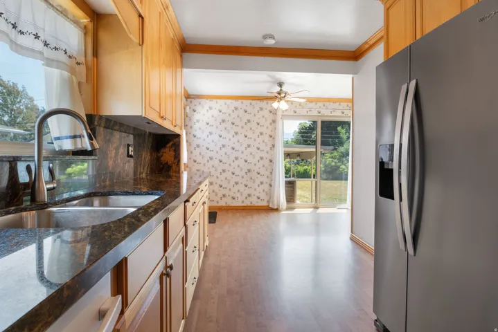 Kitchen featuring natural wood cabinetry, dark stone countertops with an integrated sink, a stainless steel refrigerator, and wood-finish flooring