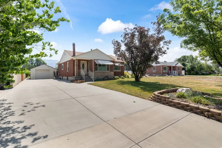 Brick exterior residence with a concrete driveway, detached garage, front lawn, and mature trees