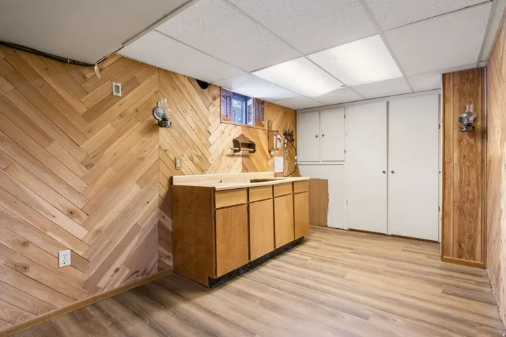 Room featuring wood-finish flooring, herringbone-patterned wood-paneled walls, built-in cabinetry with a countertop, and recessed ceiling lighting