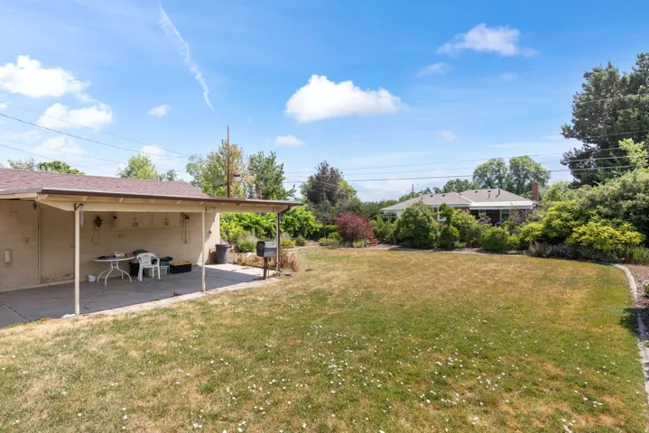 Expansive backyard featuring a covered patio with concrete flooring, a spacious lawn area, and mature perimeter landscaping