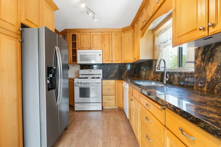 Kitchen featuring wood-finish flooring, light wood cabinetry, stone countertops, and stainless-steel appliances