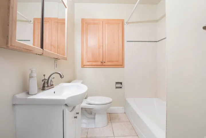 Bathroom featuring a white vanity with an integrated sink, brushed nickel faucet, light wood cabinetry, a mirrored medicine cabinet, and a bathtub with white subway tile surround