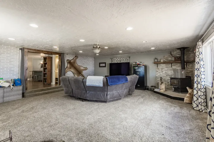 Spacious living area featuring neutral carpeting, recessed ceiling lighting, and a wood-burning stove with a stone surround