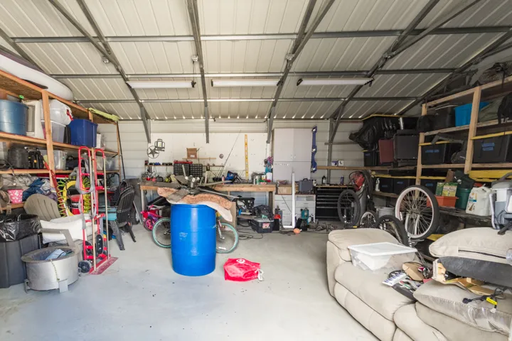Spacious metal outbuilding featuring a corrugated metal ceiling, exposed support beams, concrete flooring, and built-in shelving units