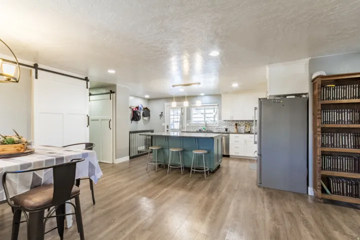 Open-concept kitchen featuring a teal island with seating, white cabinetry, stainless steel appliances, and a tiled backsplash