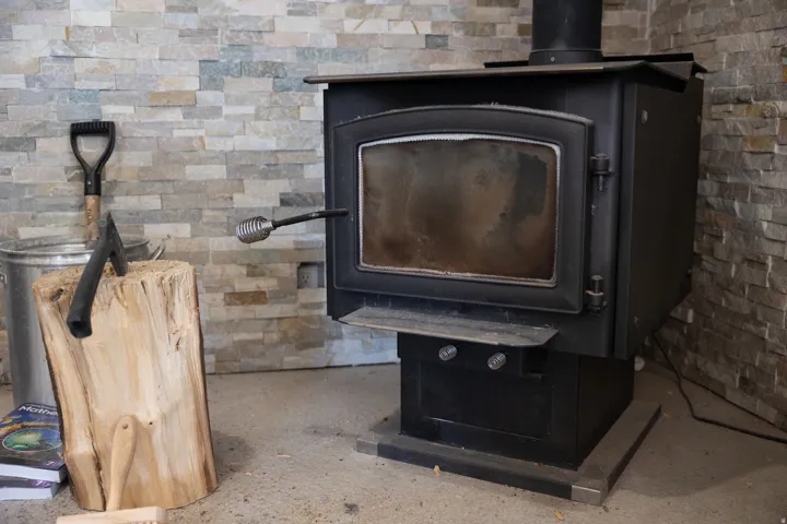 Freestanding wood-burning stove with a glass-front door, set against a stacked stone accent wall