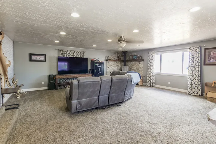Spacious room featuring neutral carpeting, recessed lighting, a ceiling fan, a window with trim, and a stone-clad fireplace with a wood mantel