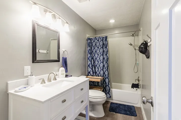 Contemporary bathroom featuring a single vanity with a white countertop and undermount sink, brushed nickel faucet, framed mirror, and a full bathtub with shower