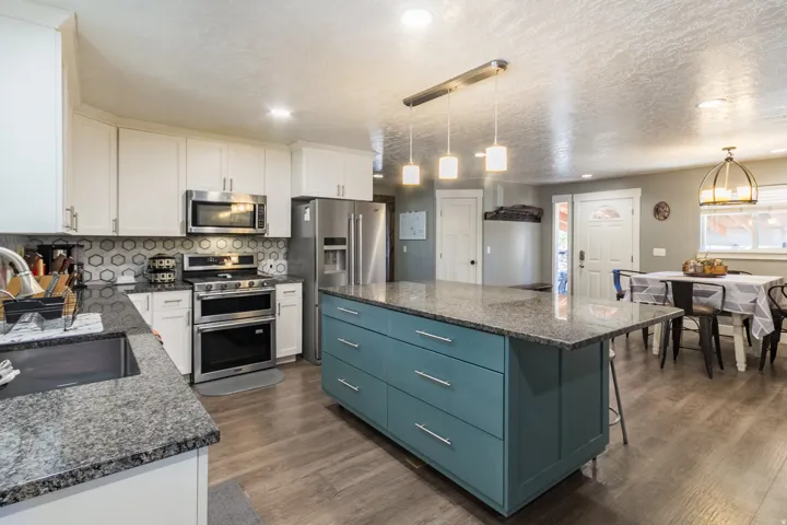 Modern kitchen featuring an expansive island with a stone-finish countertop, stainless steel appliances, white cabinetry, and wood-finish flooring