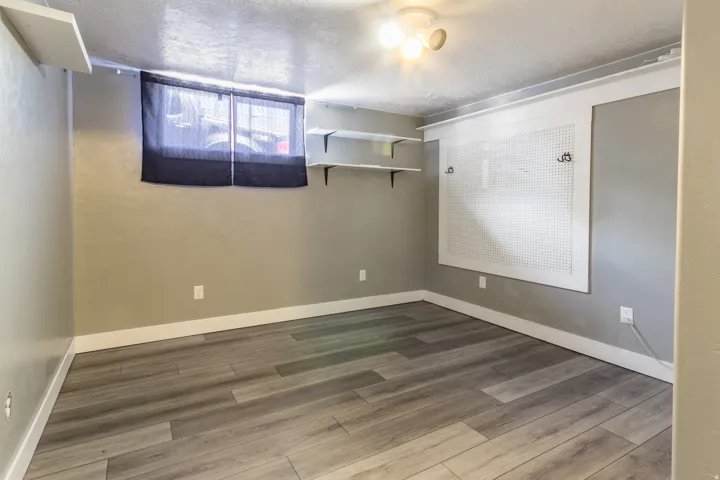 Room featuring wood-finish flooring, a window with dark blinds, and light gray walls