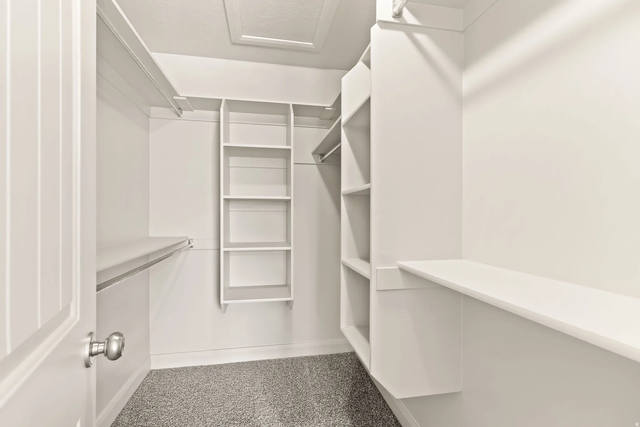 Walk-in closet featuring built-in shelving, hanging rods, an attic access panel, and neutral gray carpeting