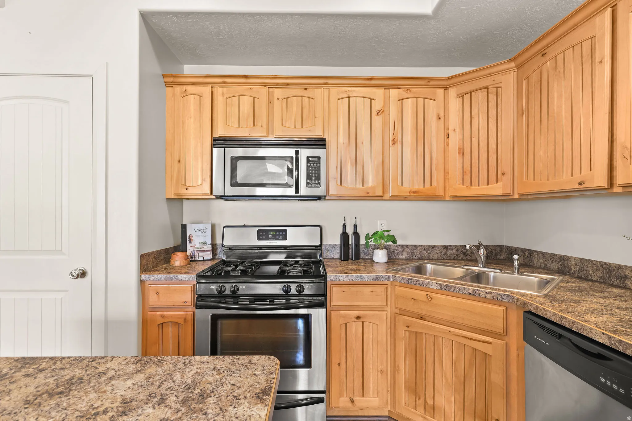 Kitchen featuring wood-finish cabinetry, stainless steel range, stainless steel microwave, double basin sink, and laminate countertops