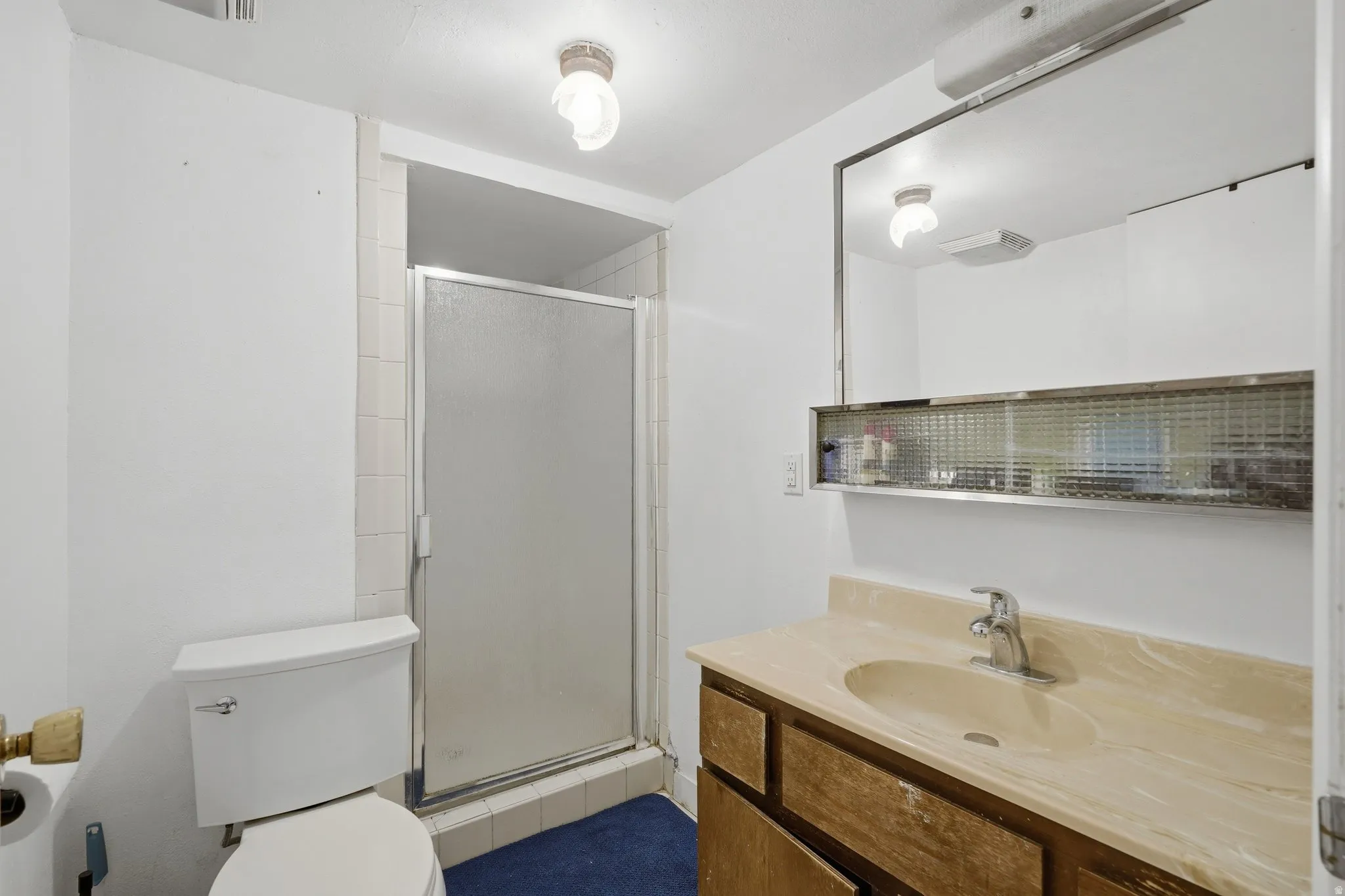 Bathroom featuring a frosted glass shower enclosure, a vanity with a light-toned countertop and integrated sink, a built-in mirror with integrated shelving, and white walls