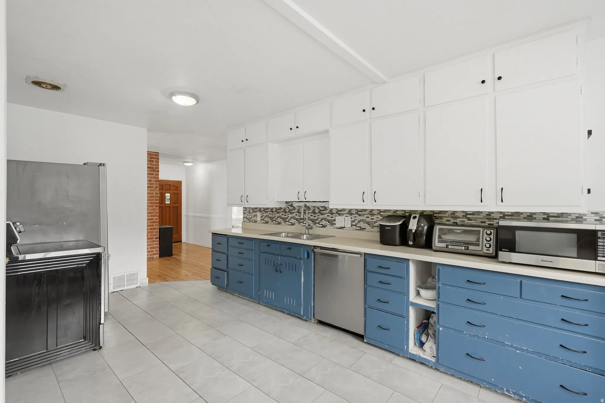 Kitchen featuring extensive white upper cabinetry, blue lower cabinetry with black hardware, a light-toned countertop, and a mosaic tile backsplash