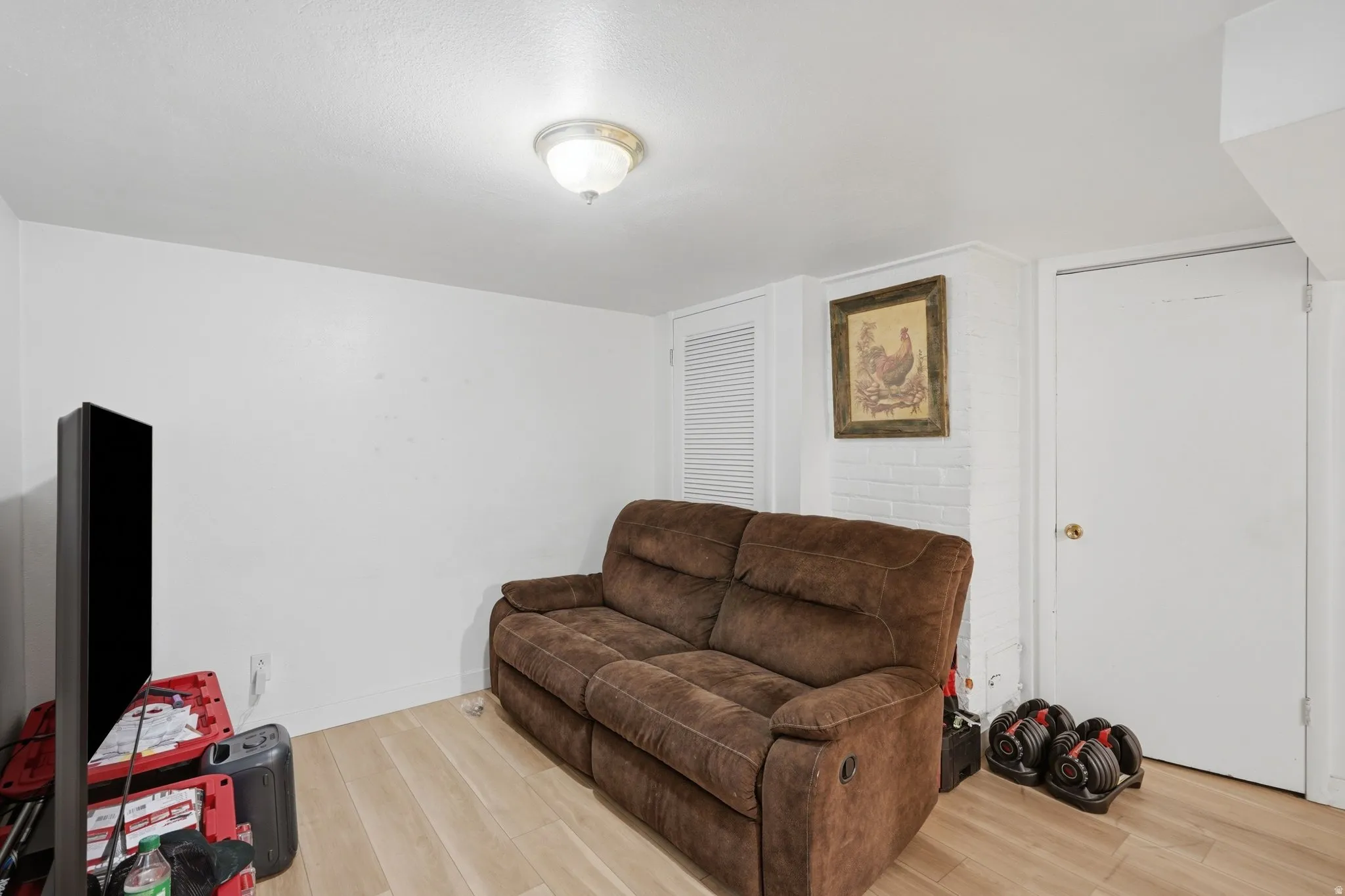 Finished room featuring wood-finish flooring, white painted walls, a flush-mount ceiling light, and a white interior door with a brass-finish knob
