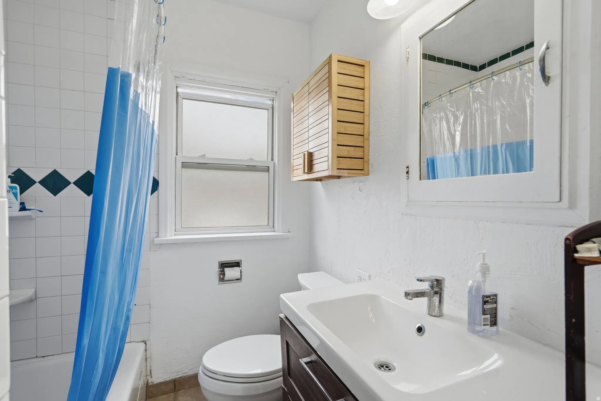 Bathroom featuring a white bathtub, ceramic wall tiling with accent diamonds, and a window with frosted glass