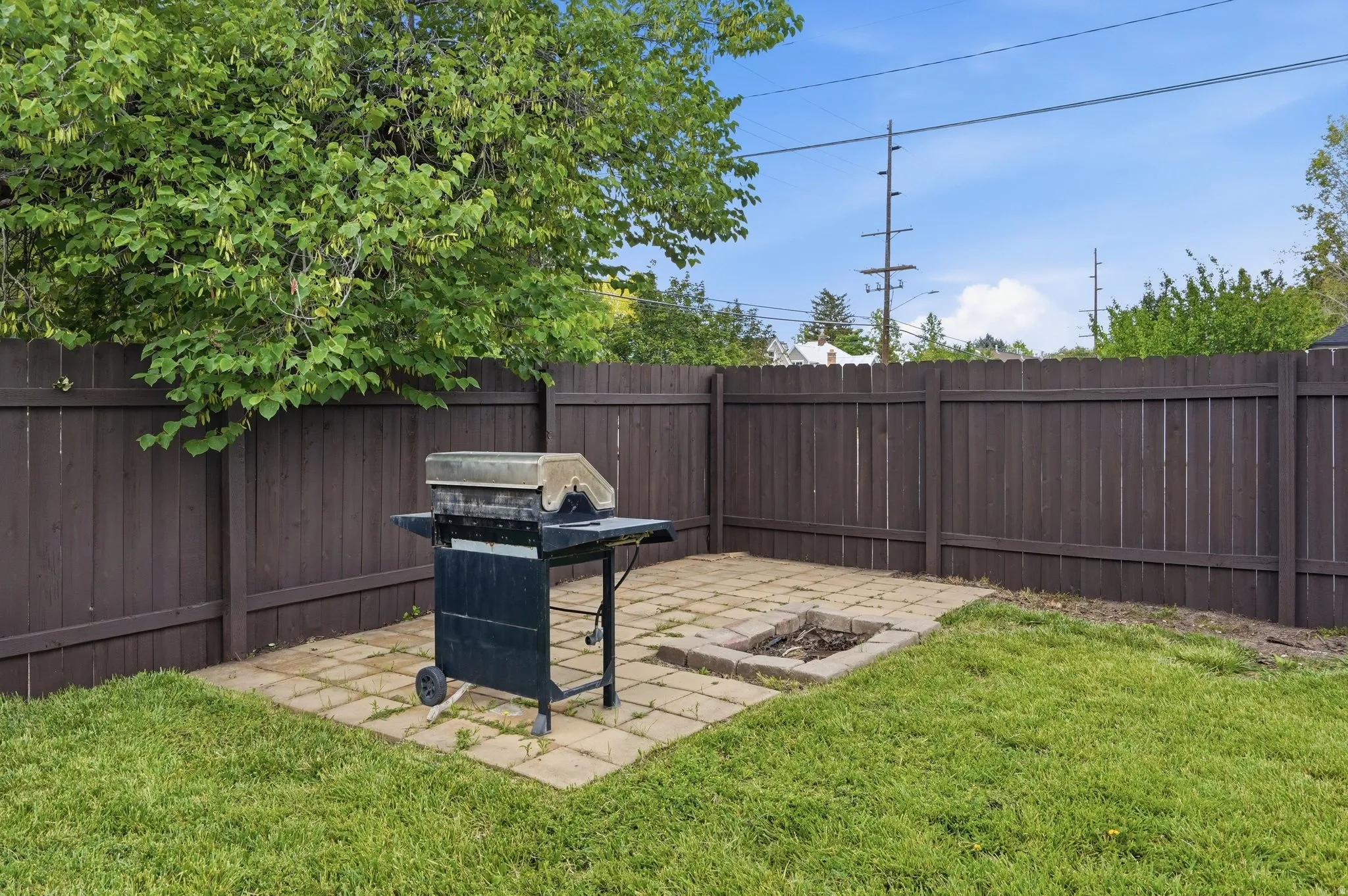 Private backyard featuring a paver patio with a built-in fire pit, surrounded by a wood privacy fence and mature trees