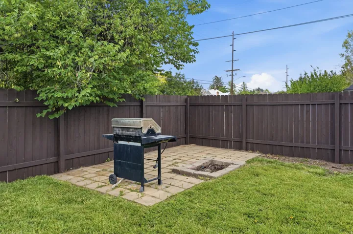 Private backyard featuring a paver patio with a built-in fire pit, surrounded by a wood privacy fence and mature trees
