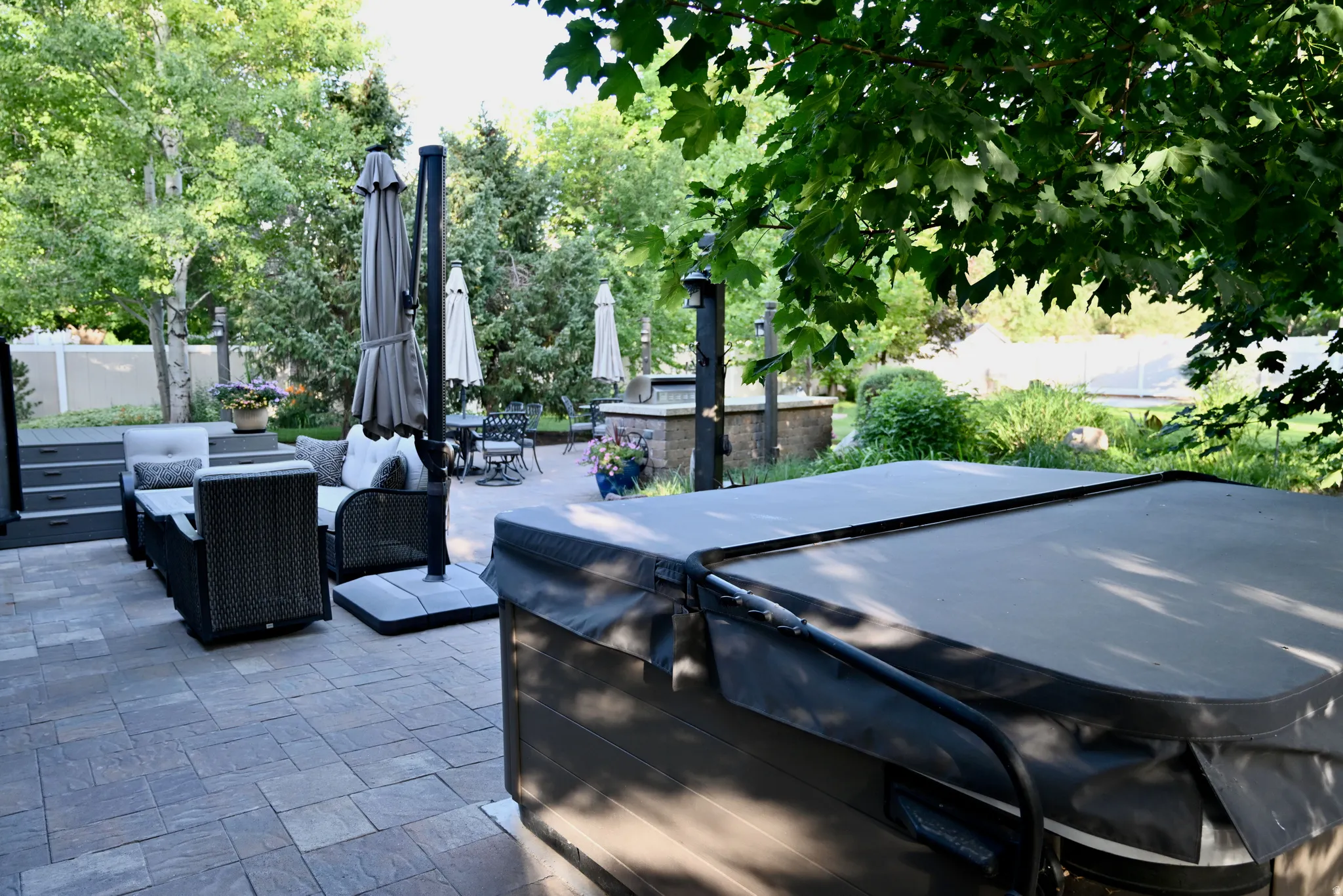 Expansive paver patio featuring a covered spa, built-in outdoor kitchen, and mature landscaping