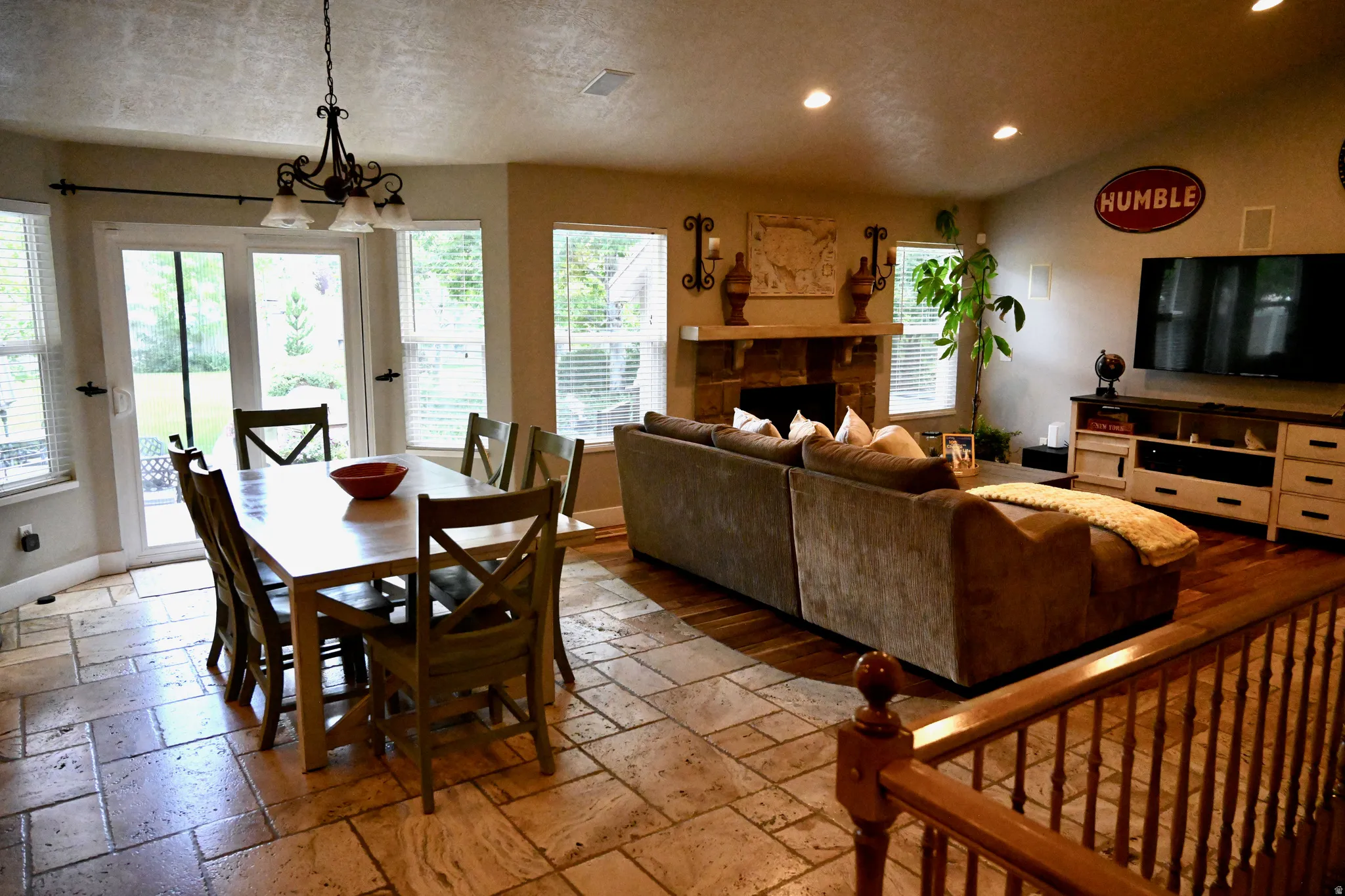 Open concept living space featuring a stone fireplace with a substantial mantel, recessed lighting, and a blend of wood-finish and stone tile flooring