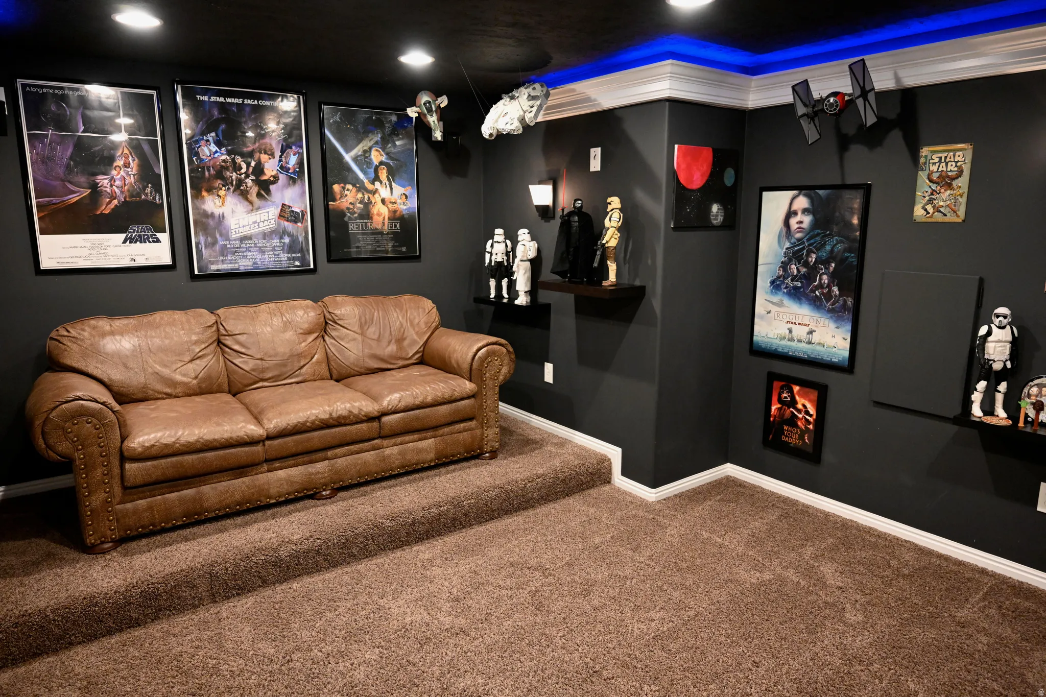 Carpeted room featuring dark walls, recessed ceiling lighting, crown molding with accent lighting, and a raised platform