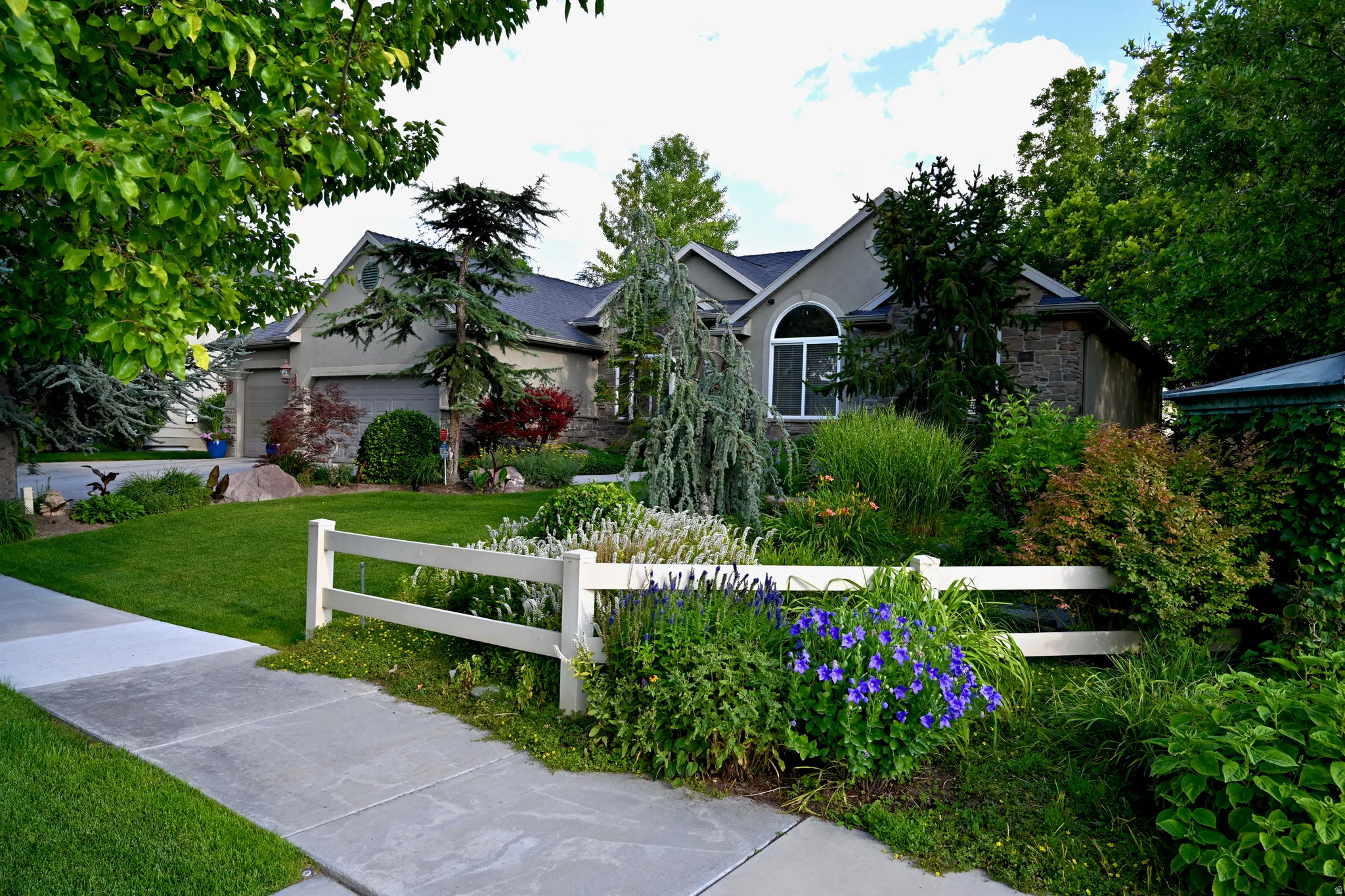 Stucco and stone exterior featuring an arched window, a two-car garage, and a manicured lawn
