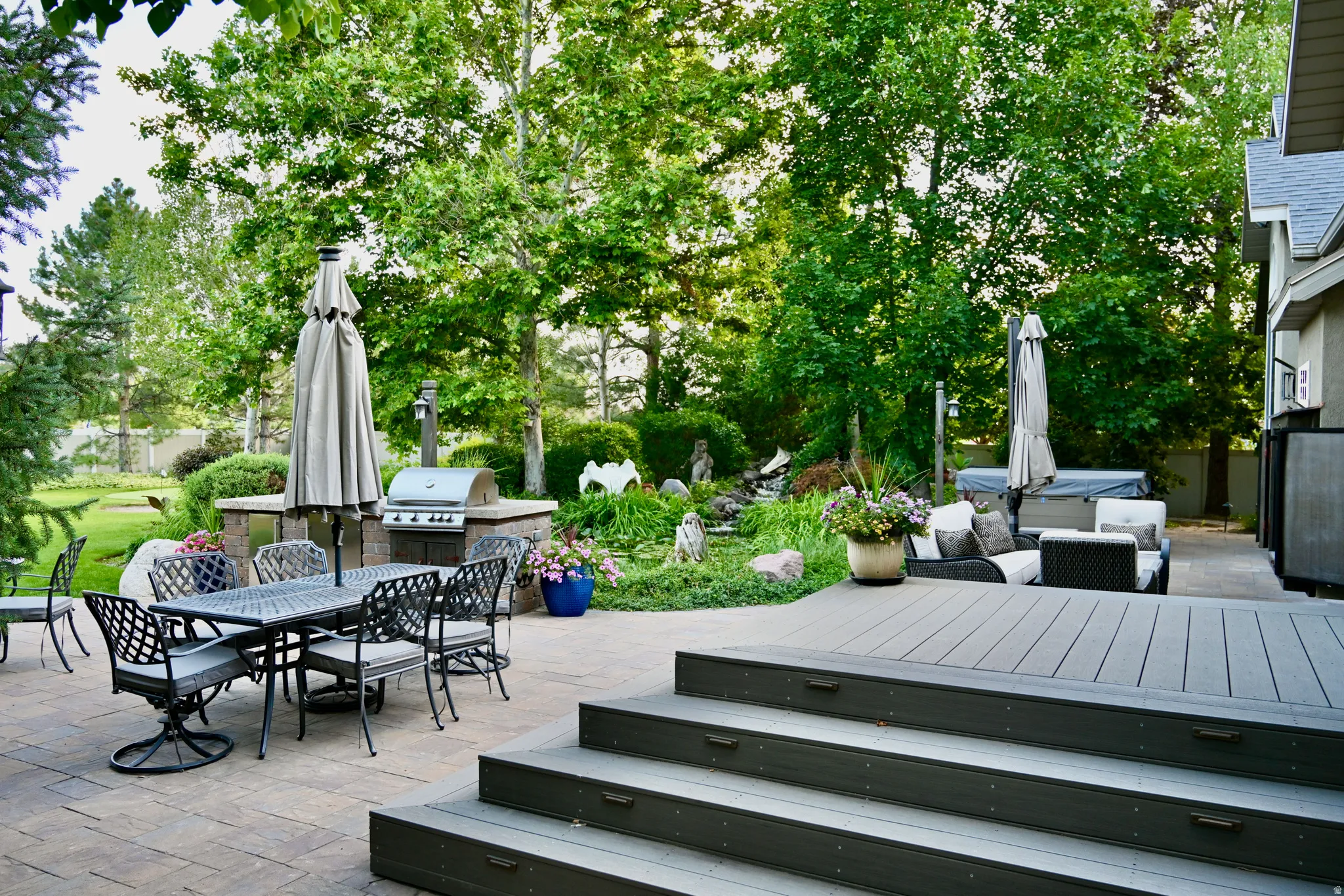 Multi-level outdoor living space featuring a composite deck with steps, a paver patio, and a built-in outdoor kitchen with a grill