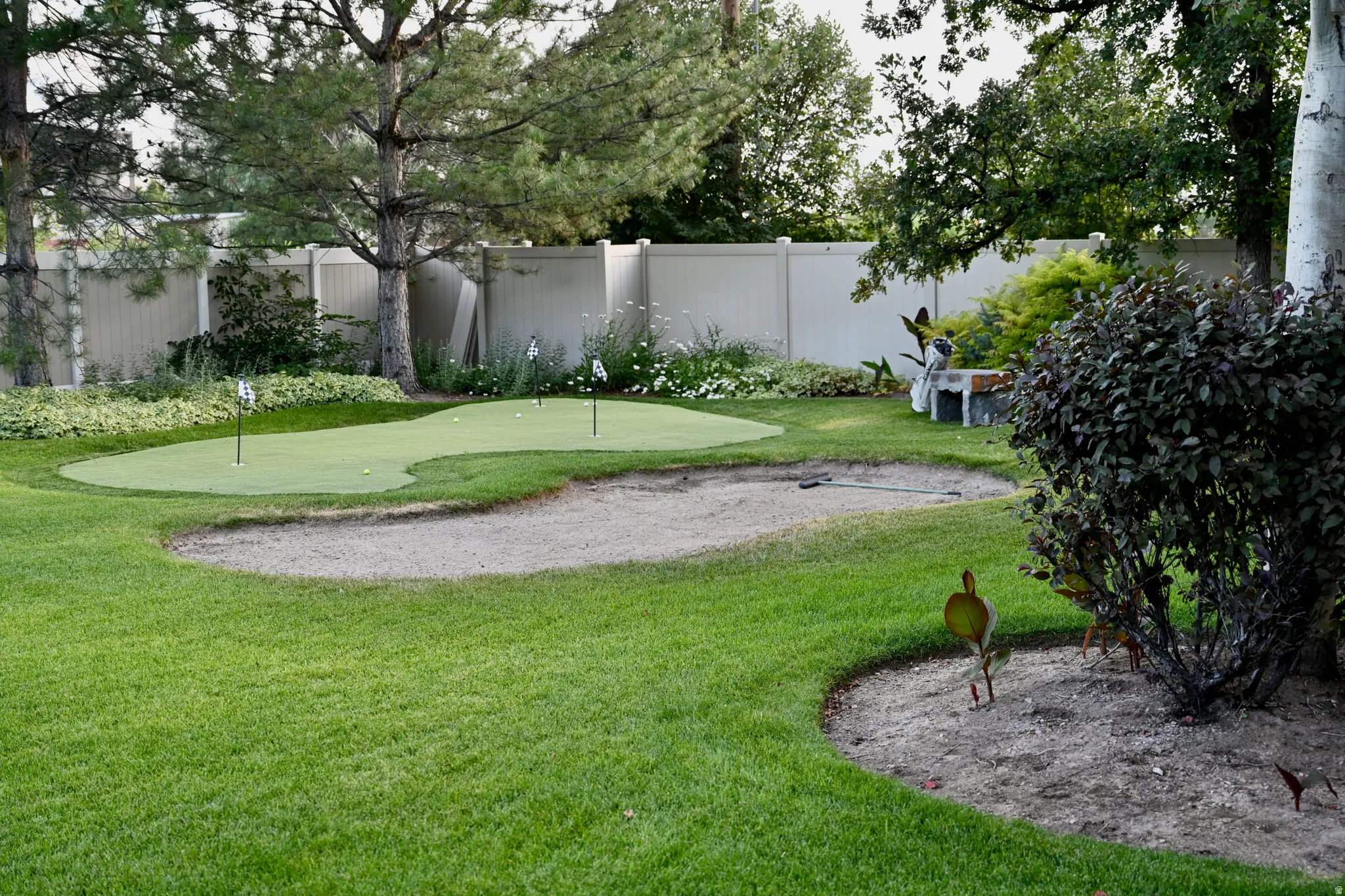 Private backyard featuring a putting green with multiple holes, a sand trap, and lush green lawn