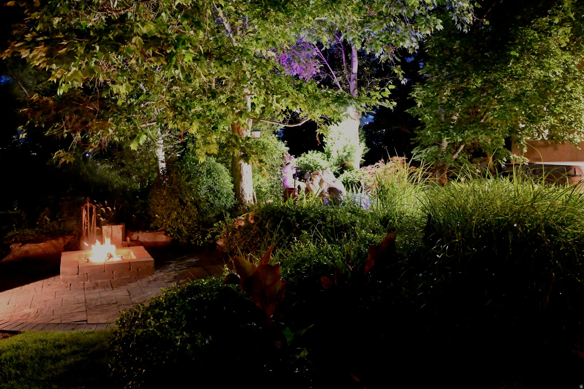 Outdoor living space featuring a brick paver patio, integrated fire pit, and extensive landscaping