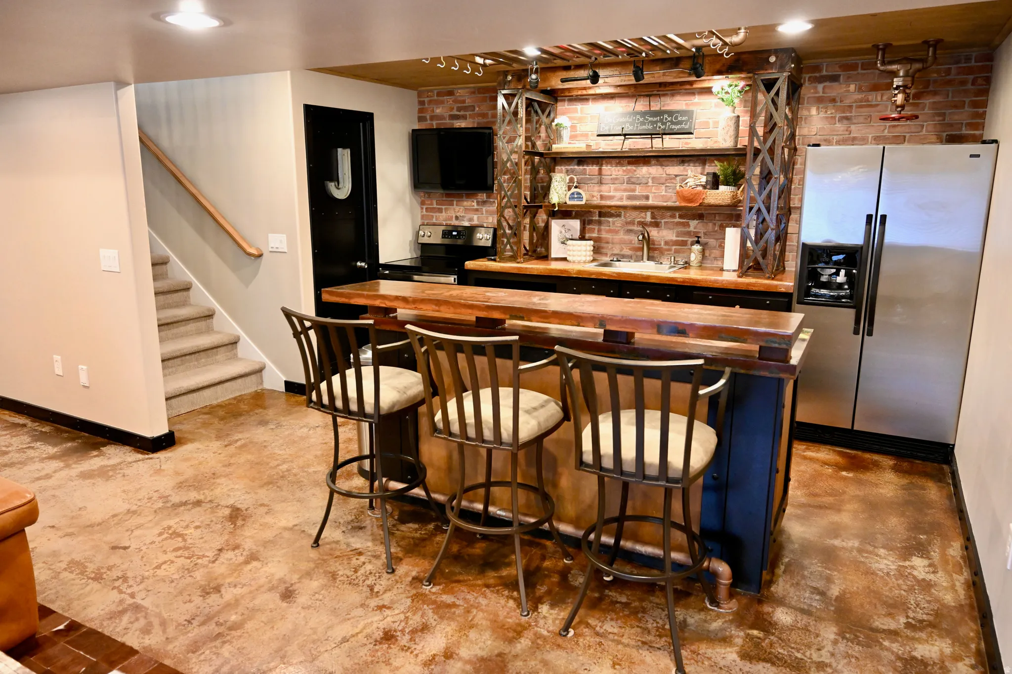 Industrial-chic wet bar featuring a wood-finish countertop, exposed brick backsplash, open shelving, and stainless steel appliances